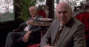 Movie still from “Prizzi's Honor” (1985), directed by John Huston – Two men in suits and ties sitting next to each other; Medium shot, Low angle