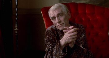 Movie still from “Prizzi's Honor” (1985), directed by John Huston – An older man sitting on a red chair with his hands crossed; Close Up shot, Low angle