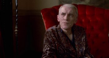 Movie still from “Prizzi's Honor” (1985), directed by John Huston – An older man sitting on a red chair; Medium shot, Over the shoulder angle