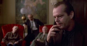 Movie still from “Prizzi's Honor” (1985), directed by John Huston – A man talking on a cell phone while sitting on a couch; Medium shot, Over the shoulder angle