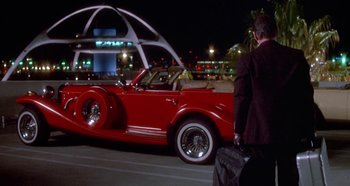 Movie still from “Prizzi's Honor” (1985), directed by John Huston – A man standing next to a red classic car; Wide shot, Low angle