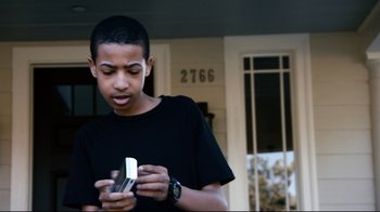 Movie still from “Project X” (2012), directed by Nima Nourizadeh – A young man holding a cell phone while standing in front of a house; Medium shot, Low angle