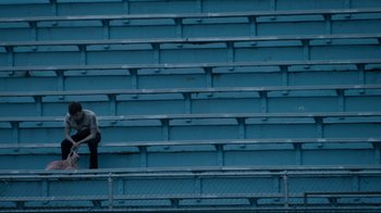 Movie still from “Project X” (2012), directed by Nima Nourizadeh – A man sitting on a bleacher in front of bleachers; Extreme Wide shot, High angle