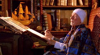 Movie still from “Prospero's Books” (1991), directed by Peter Greenaway – An old man sitting in a chair writing on a piece of paper; Medium shot, High angle