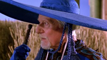 Movie still from “Prospero's Books” (1991), directed by Peter Greenaway – An old man with a blue hat and a beard holding an umbrella over his head; Close Up shot, Over the shoulder angle
