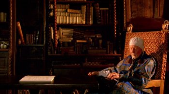 Movie still from “Prospero's Books” (1991), directed by Peter Greenaway – An older man sitting in front of a book shelf; Medium shot, Low angle