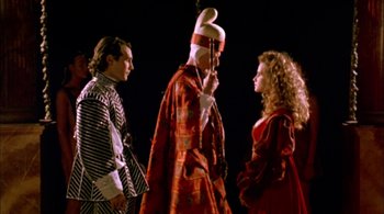 Movie still from “Prospero's Books” (1991), directed by Peter Greenaway – A man in a red coat and a woman in a red dress stand next to a man; Medium shot, Low angle