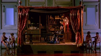 Movie still from “Prospero's Books” (1991), directed by Peter Greenaway – A man sitting in a chair in front of a book shelf; Wide shot, Low angle