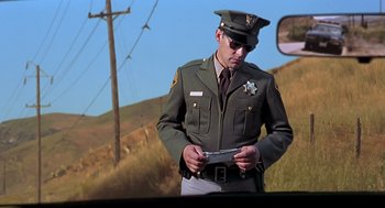 Movie still from “Psycho” (1998), directed by Gus Van Sant – A man in a police uniform is holding papers; Medium shot, Low angle