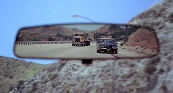 Movie still from “Psycho” (1998), directed by Gus Van Sant – The reflection of a police car in the rear view mirror of a truck; Wide shot, Low angle