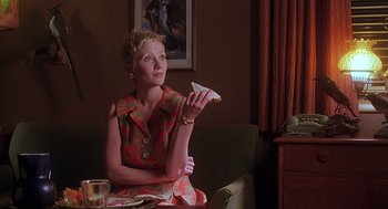 Movie still from “Psycho” (1998), directed by Gus Van Sant – A woman sitting on a couch holding a piece of food; Medium shot, Low angle
