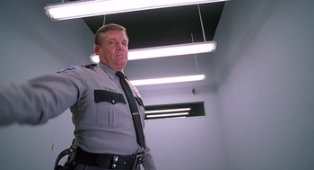 Movie still from “Psycho” (1998), directed by Gus Van Sant – A man in a police uniform standing in a room; Medium shot, Low angle