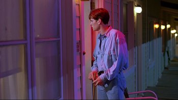 Movie still from “Psycho IV: The Beginning” (1990), directed by Mick Garris – A man standing in front of a building holding a gun; Medium shot, Low angle