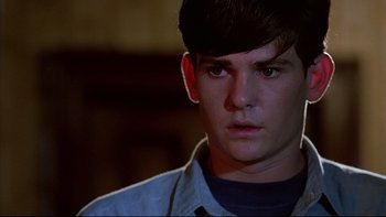 Movie still from “Psycho IV: The Beginning” (1990), directed by Mick Garris – A young man looking at the camera in a dark room; Close Up shot, Over the shoulder angle