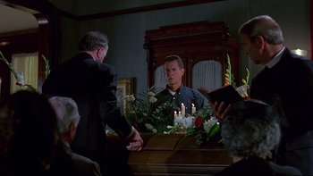 Movie still from “Psycho IV: The Beginning” (1990), directed by Mick Garris – A man standing in front of a casket with candles; Medium shot, Over the shoulder angle
