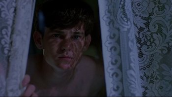 Movie still from “Psycho IV: The Beginning” (1990), directed by Mick Garris – A young man looking out of a window at night; Close Up shot, Low angle