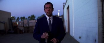 Movie still from “Punch-Drunk Love” (2002), directed by Paul Thomas Anderson – A man in a blue suit holding a camera; Medium shot, Over the shoulder angle