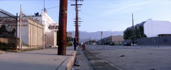Movie still from “Punch-Drunk Love” (2002), directed by Paul Thomas Anderson – A man standing on the side of the road near a power pole; Extreme Wide shot, High angle