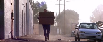 Movie still from “Punch-Drunk Love” (2002), directed by Paul Thomas Anderson – A man walking down a street carrying a box; Wide shot, Low angle