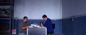 Movie still from “Punch-Drunk Love” (2002), directed by Paul Thomas Anderson – Two men sitting at a table in front of each other; Wide shot, Low angle