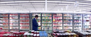 Movie still from “Punch-Drunk Love” (2002), directed by Paul Thomas Anderson – A man in a blue suit looking at a book in a store; Wide shot, Low angle