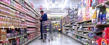Movie still from “Punch-Drunk Love” (2002), directed by Paul Thomas Anderson – A man in a suit is shopping in a grocery store; Wide shot, High angle