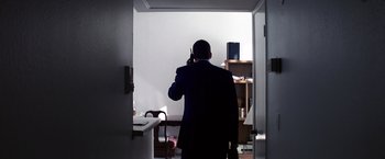 Movie still from “Punch-Drunk Love” (2002), directed by Paul Thomas Anderson – A man standing in a doorway talking on a cell phone; Wide shot, High angle