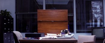 Movie still from “Punch-Drunk Love” (2002), directed by Paul Thomas Anderson – A wooden box sitting on top of a desk; Wide shot, High angle