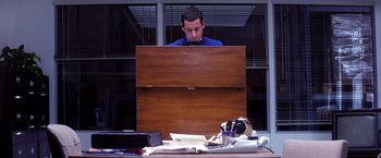 Movie still from “Punch-Drunk Love” (2002), directed by Paul Thomas Anderson – A man sitting in front of an open wooden box; Medium shot, High angle