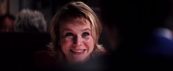 Movie still from “Punch-Drunk Love” (2002), directed by Paul Thomas Anderson – A woman smiling for the camera; Close Up shot, Over the shoulder angle