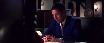 Movie still from “Punch-Drunk Love” (2002), directed by Paul Thomas Anderson – A man sitting at a table looking at his cell phone; Close Up shot, Over the shoulder angle