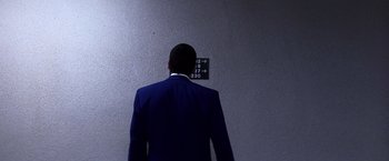 Movie still from “Punch-Drunk Love” (2002), directed by Paul Thomas Anderson – A man in a suit and tie standing in front of a wall; Medium shot, Low angle