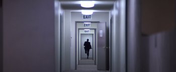 Movie still from “Punch-Drunk Love” (2002), directed by Paul Thomas Anderson – A person walking down a hallway with exit signs; Extreme Wide shot, High angle