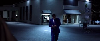 Movie still from “Punch-Drunk Love” (2002), directed by Paul Thomas Anderson – A man in a suit and tie looking at his cell phone; Wide shot, Low angle