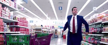 Movie still from “Punch-Drunk Love” (2002), directed by Paul Thomas Anderson – A man in a blue suit and a red tie in a grocery store; Wide shot, Low angle