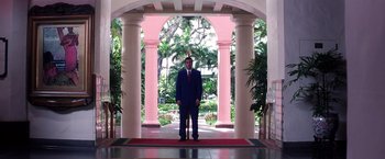 Movie still from “Punch-Drunk Love” (2002), directed by Paul Thomas Anderson – A man in a blue suit standing in front of a pink building; Wide shot, Low angle