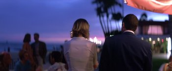 Movie still from “Punch-Drunk Love” (2002), directed by Paul Thomas Anderson – A woman in a white jacket standing in front of palm trees at night; Medium shot, Over the shoulder angle