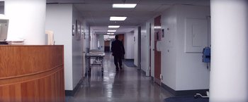 Movie still from “Punch-Drunk Love” (2002), directed by Paul Thomas Anderson – A man walking down a hallway with a hospital bed; Wide shot, High angle