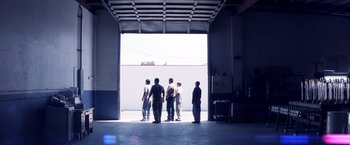 Movie still from “Punch-Drunk Love” (2002), directed by Paul Thomas Anderson – A group of people standing in a garage; Wide shot, Low angle