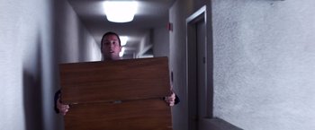 Movie still from “Punch-Drunk Love” (2002), directed by Paul Thomas Anderson – A man holding a wooden box in a hallway; Medium shot, High angle
