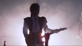 Movie still from “Purple Rain” (1984), directed by Albert Magnoli – A man in a white shirt is holding a guitar; Wide shot, Low angle