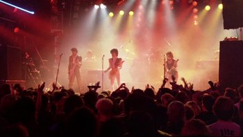 Movie still from “Purple Rain” (1984), directed by Albert Magnoli – A group of people on a stage in front of an audience; Wide shot, Low angle