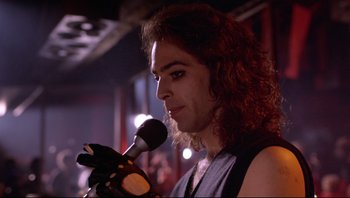 Movie still from “Purple Rain” (1984), directed by Albert Magnoli – A man with long curly hair is holding a microphone; Close Up shot, Low angle