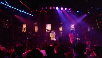 Movie still from “Purple Rain” (1984), directed by Albert Magnoli – A group of people in a room with lights on; Wide shot, Low angle