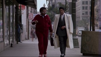 Movie still from “Purple Rain” (1984), directed by Albert Magnoli – Two people walking down the street wearing red and white; Wide shot, Low angle