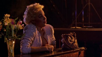 Movie still from “Purple Rain” (1984), directed by Albert Magnoli – A woman sitting at a table with a purse; Medium shot, Over the shoulder angle