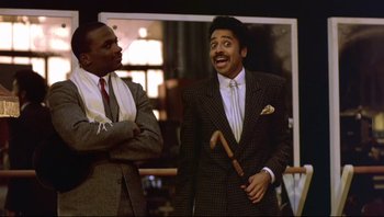 Movie still from “Purple Rain” (1984), directed by Albert Magnoli – Two men in suits and ties are laughing; Medium shot, Low angle