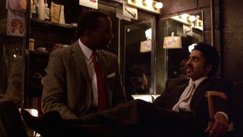 Movie still from “Purple Rain” (1984), directed by Albert Magnoli – Two men in suits are talking to each other; Medium shot, Over the shoulder angle