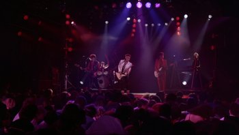 Movie still from “Purple Rain” (1984), directed by Albert Magnoli – A group of people on a stage with lights in the background; Wide shot, Low angle