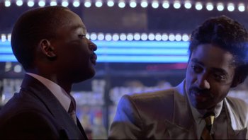 Movie still from “Purple Rain” (1984), directed by Albert Magnoli – Two men in suits are talking in front of a neon sign; Close Up shot, Over the shoulder angle